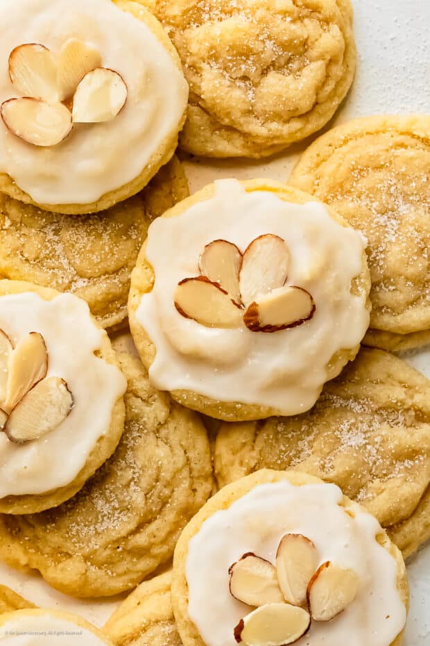Close-up photo of a sugar cookie almond topped with vanilla icing and slivered almonds.