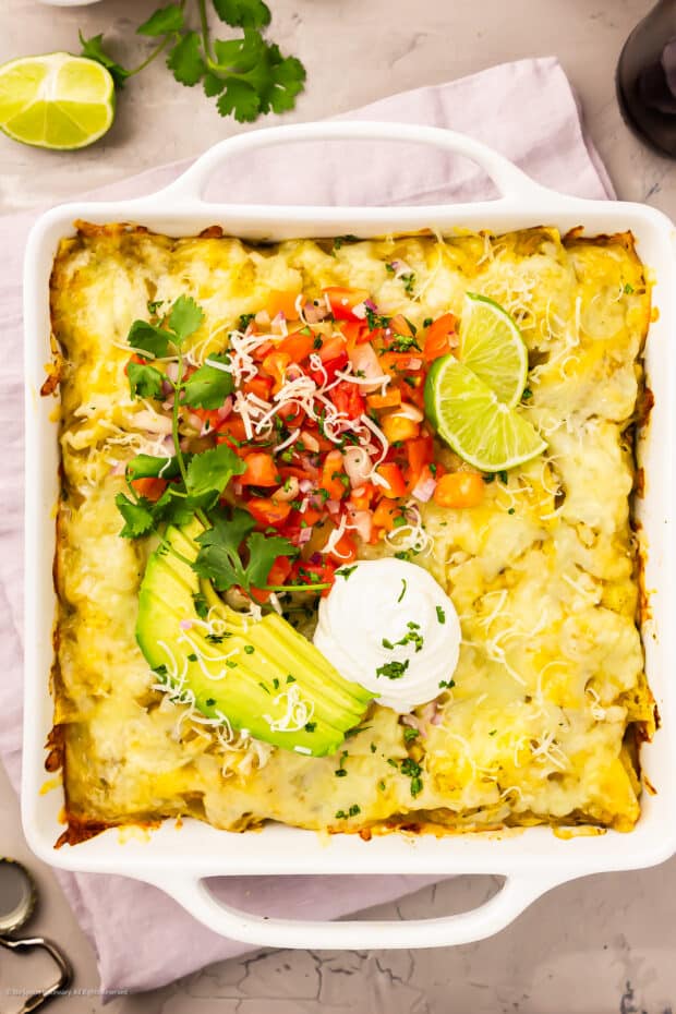 Overhead photo of a baked green chicken enchilada casserole in a white casserole baking dish.