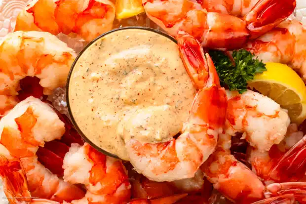 Overhead photo of prepared remoulade recipe in a glass serving bowl with cocktail shrimp surrounding the bowl.