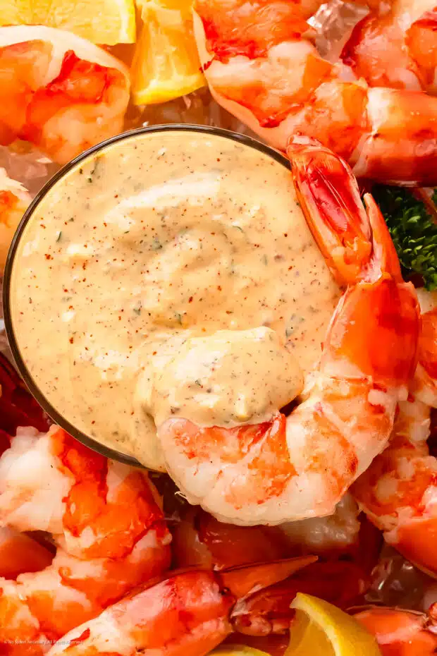 Close-up photo of sauce remoulade in a glass bowl with a jumbo cocktail shrimp resting on the sauce.