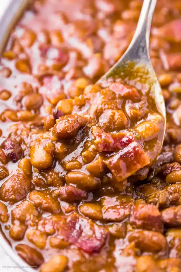 Action photo of a spoon lifting baked beans bacon from a pot.