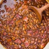 Overhead photo of baked beans with bacon in a large white pot with a wood serving spoon.