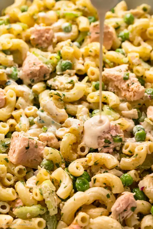 Close-up action photo of dressing being drizzled over macaroni with tuna salad.