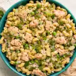 Overhead photo of tuna salad with macaroni and fresh herbs in a teal serving bowl.