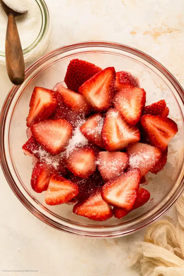 Overhead photo of fresh strawberries sprinkled with sugar in a glass bowl.