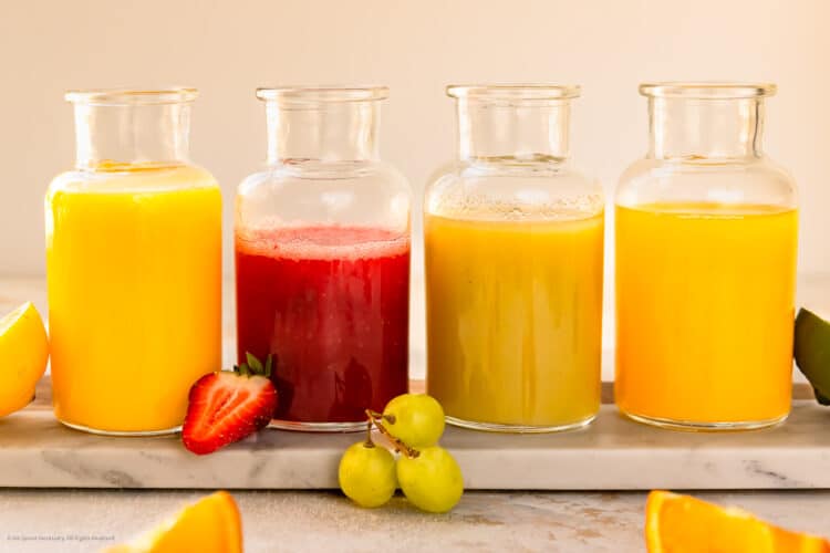 Straight on photo of four fruit purees in glass storage jars.