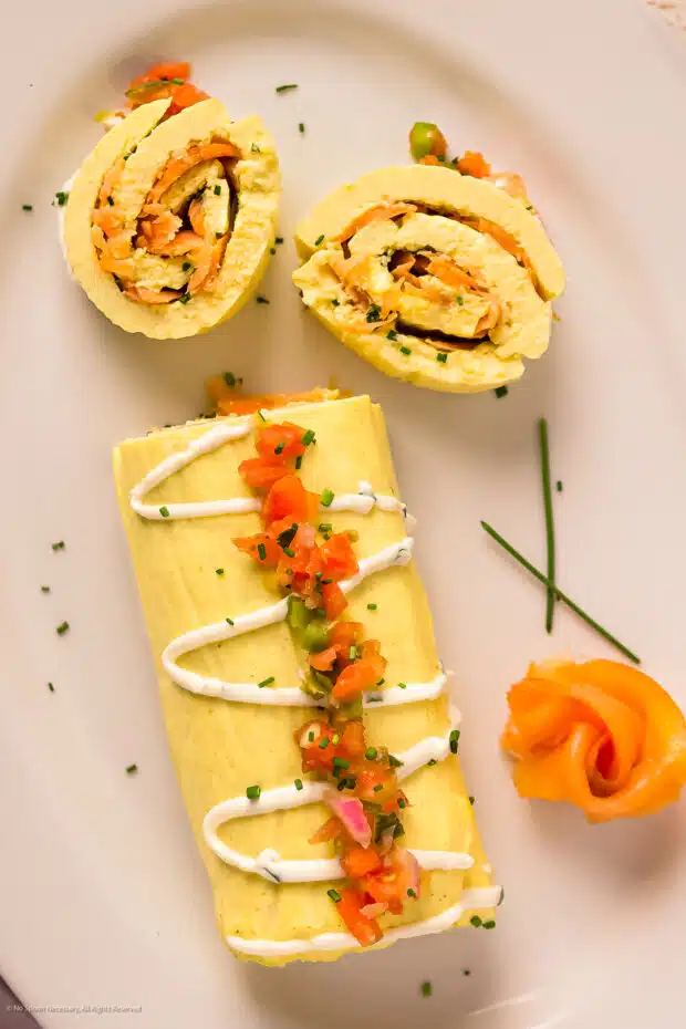 Overhead photo of a rolled omelette with smoked salmon and chives on a white platter.