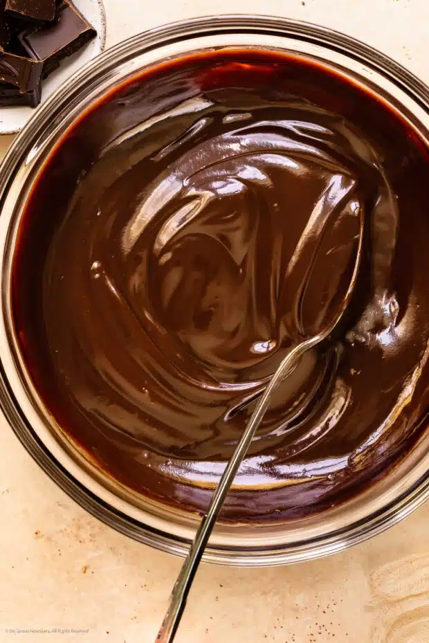 Action photo of a spoon stirring homemade chocolate sauce in a bowl.