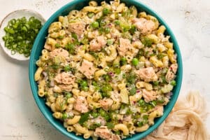 Overhead photo of tuna salad with macaroni and fresh herbs in a teal serving bowl.