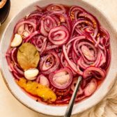 Photo of a quick pickled red onion with garlic, bay leaf, and lemon peel in a white bowl