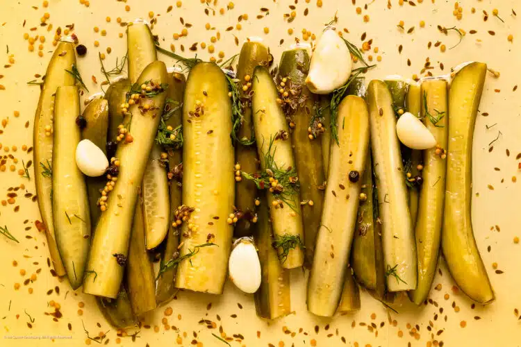 Overhead photo of refrigerator dill pickles with garlic on a white kitchen tray.