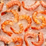 Overhead photo of six cleaned shrimp surrounded by six raw shrimp still in their shell.