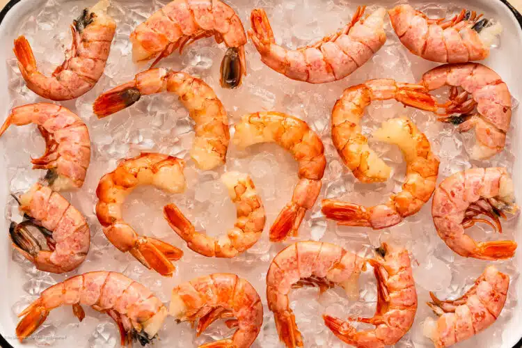 Overhead photo of six cleaned shrimp surrounded by six raw shrimp still in their shell.