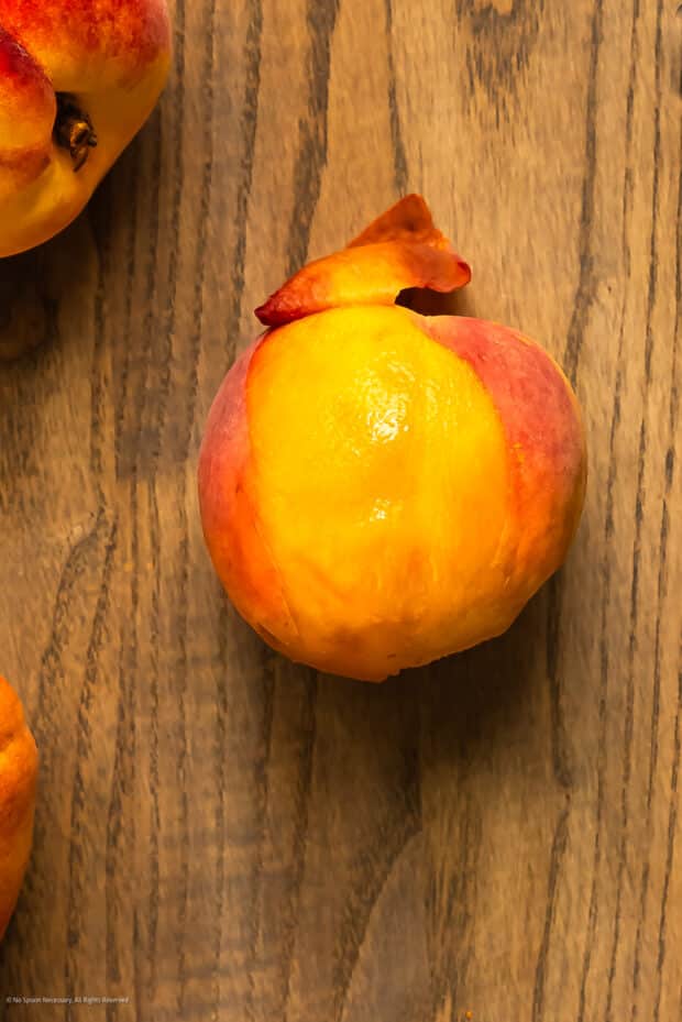 Close-up photo of a partially peeled peach on a cutting board.