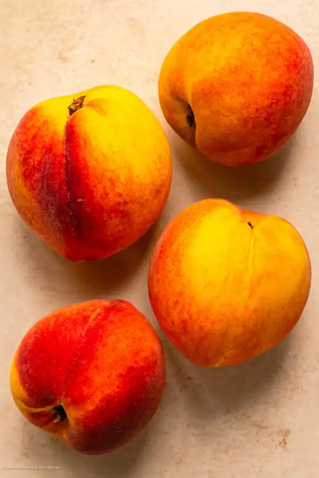 Overhead photo of four ripe peaches on a kitchen counter.