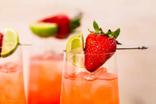 Close-up photo of the fresh strawberry garnish on a vodka drink with strawberry syrup.
