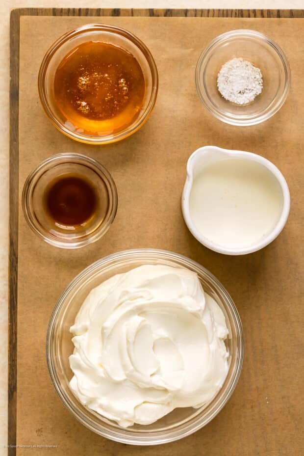 Overhead photo of Greek yogurt, heavy cream, kosher salt, pure vanilla extract, and honey neatly arranged on a kitchen tray.