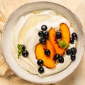 Overhead photo of whipped yogurt topped with peaches and blueberries in a white bowl.