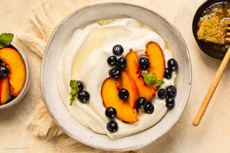 Overhead photo of whipped yogurt topped with peaches and blueberries in a white bowl.