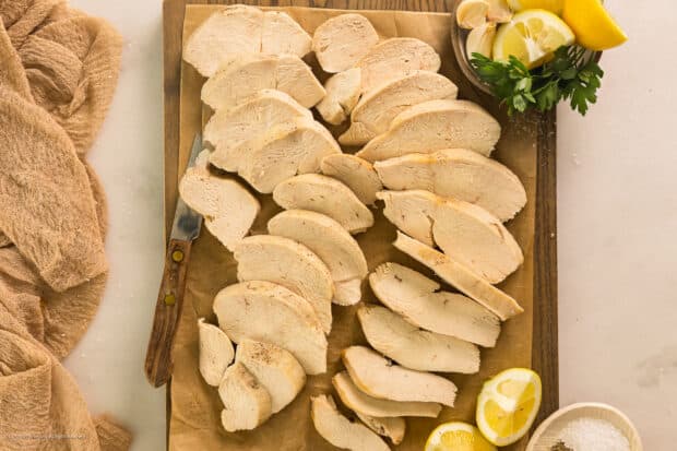 Overhead photo of a pound of sliced and perfectly poached chicken breasts arranged on a wood cutting board.
