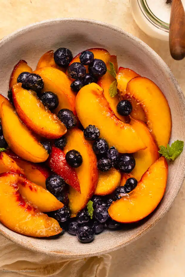 Overhead photo of macerated peaches and blueberries with fresh mint in a white bowl.