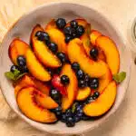 Overhead photo of a bowl of macerating fruit with a jar of sugar next the the bowl.