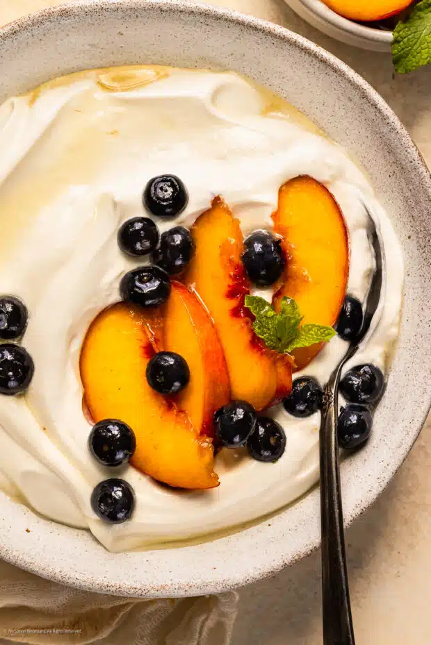 Overhead photo of soft, sugar soaked peaches and blueberries served over yogurt.