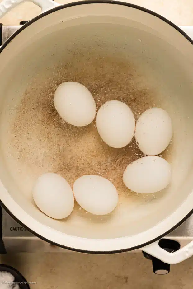 Action photo of a half dozen eggs boiling in a large pot of water.