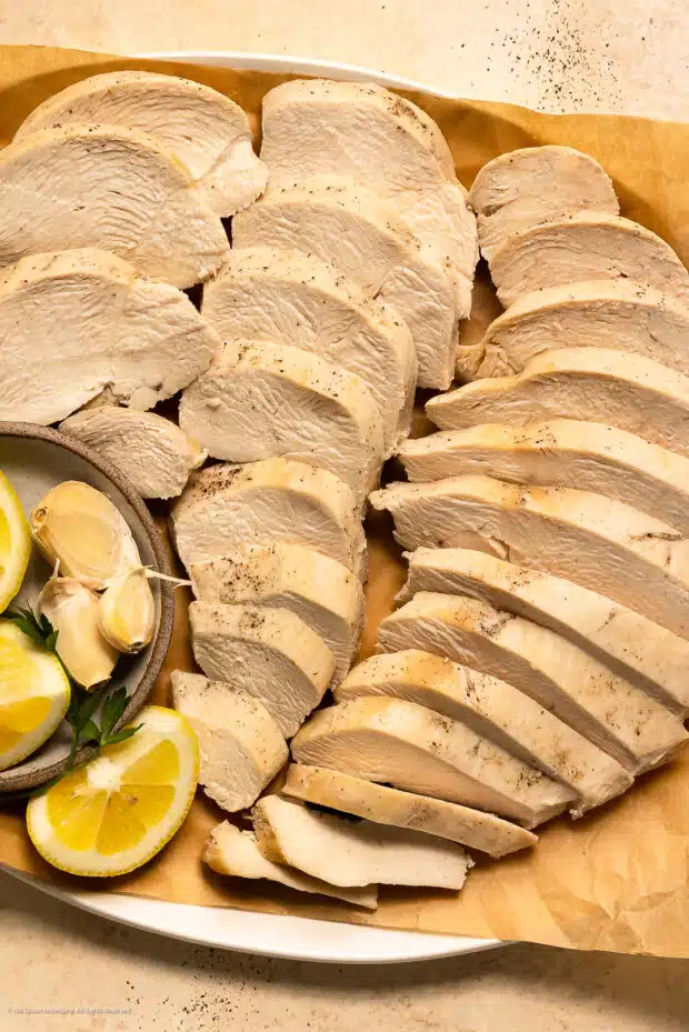 Overhead photo of thinly sliced chicken breasts poached, thinly sliced, and arranged on a serving platter.