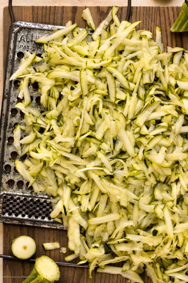 Overhead photo of riced zucchini and a grater on a cutting board.