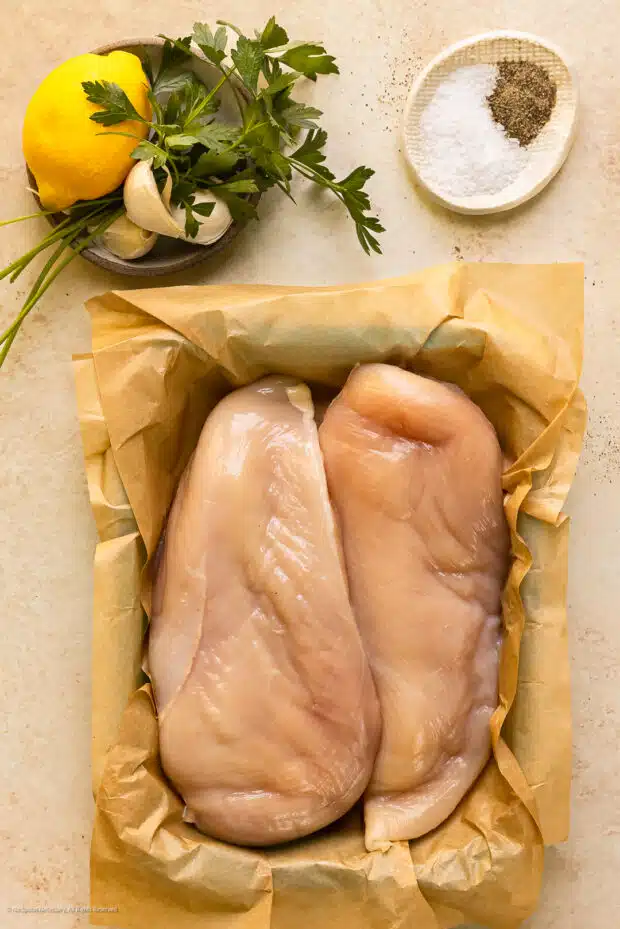 Overhead photo of the handful of ingredients you need to poach chicken - chicken breasts, salt, pepper, and optional poaching liquid flavoring ingredients.