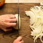 Overhead action photo of a hand holding a Chef's knife and cutting onion into slices.