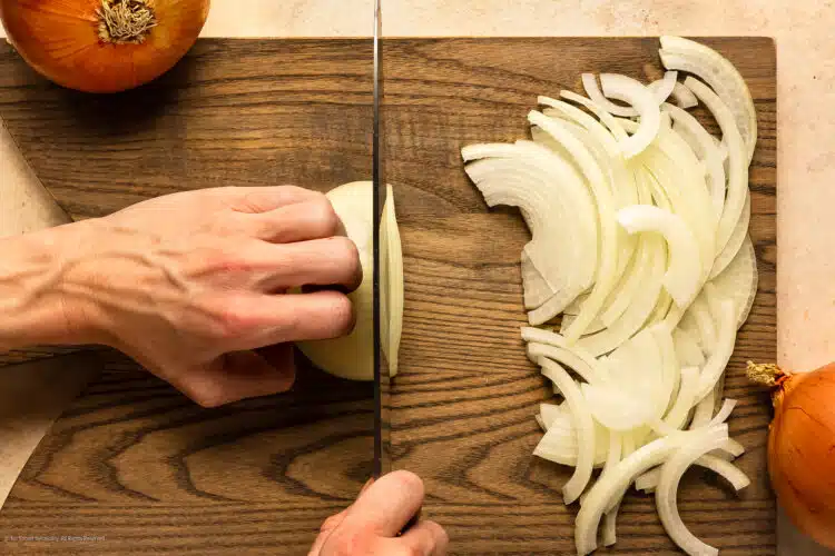Overhead action photo of a hand holding a Chef's knife and cutting onion into slices.