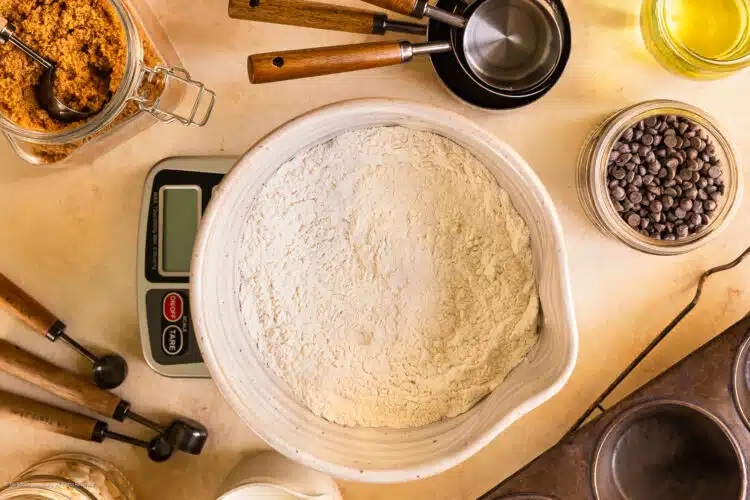 Overhead photo of a bowl of flour on a digital baking scale with measuring cups, measuring spoons, and liquid measures surrounding the scale.