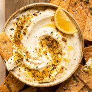 Overhead photo of a bowl of whipped ricotta topped with lemon zest and fresh herbs with crackers on the side of the bowl.