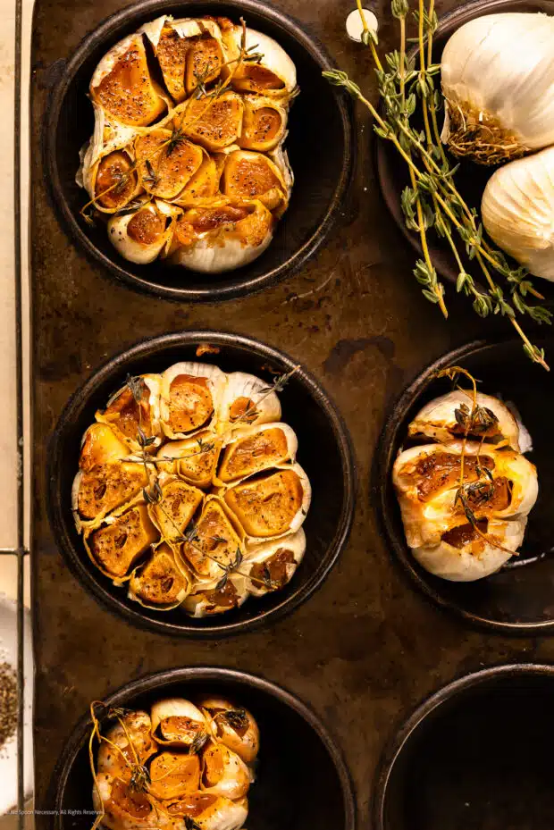 Overhead photo of roasted garlic bulb in a muffin tin.