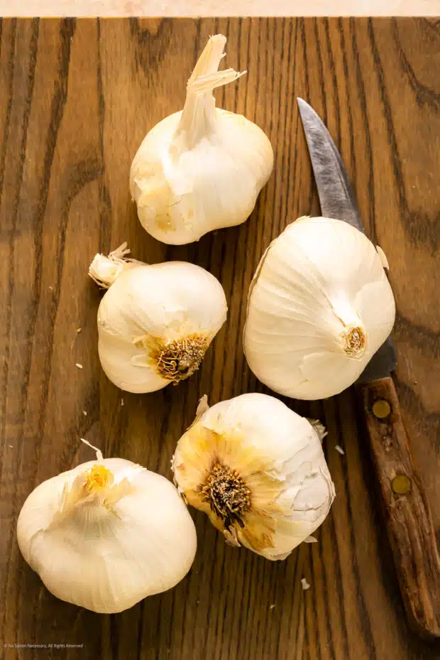 Overhead photo of five raw bulbs of garlic on a wood cutting board.