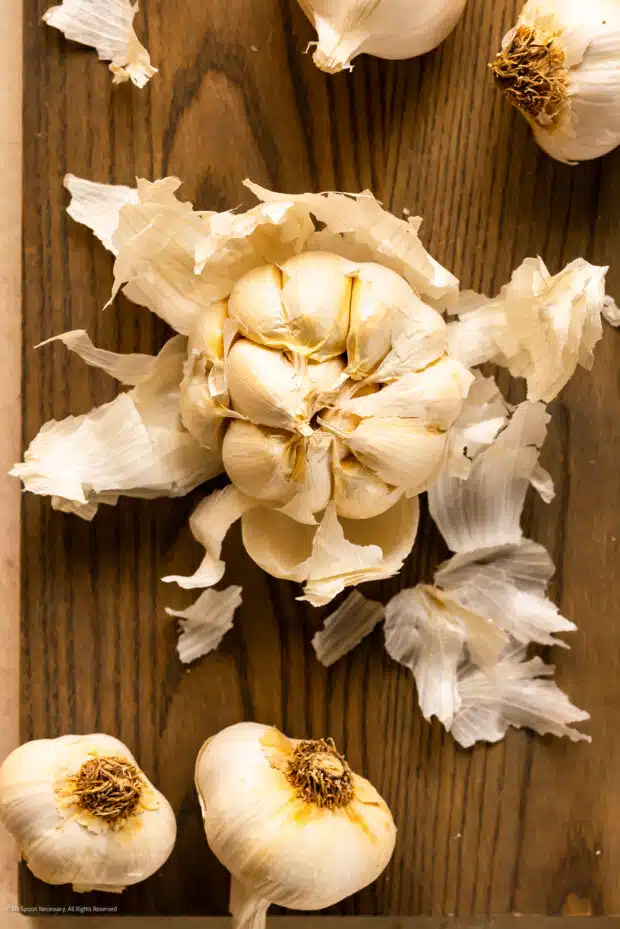 Overhead photo of a partially peeled garlic bulb on a wood cutting board.