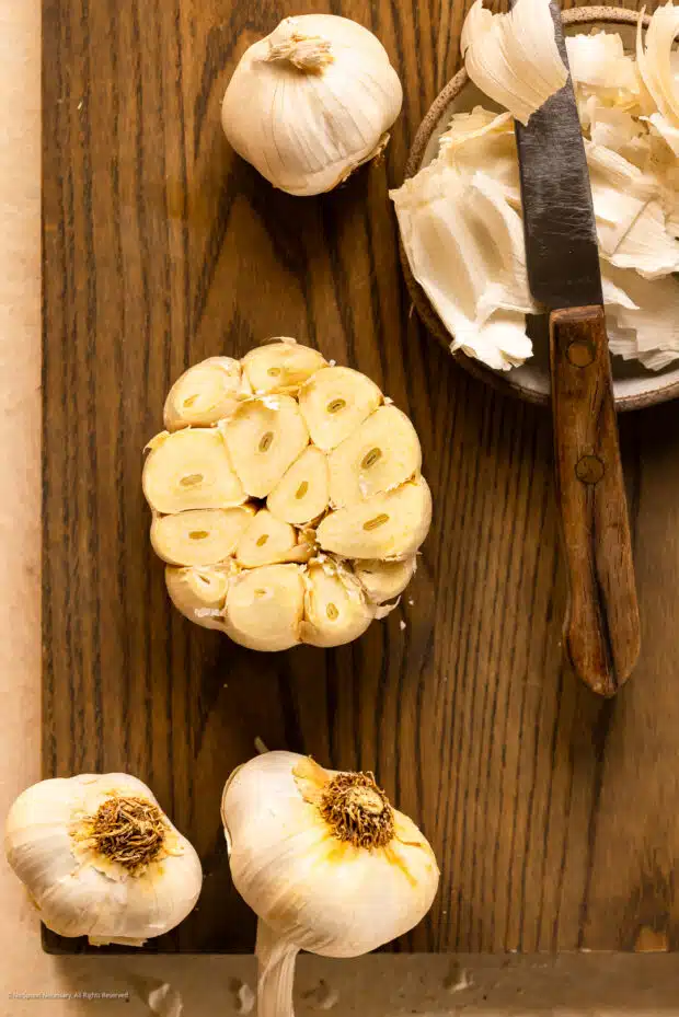 Overhead photo illustrating how to prepare raw garlic for roasting in an oven.