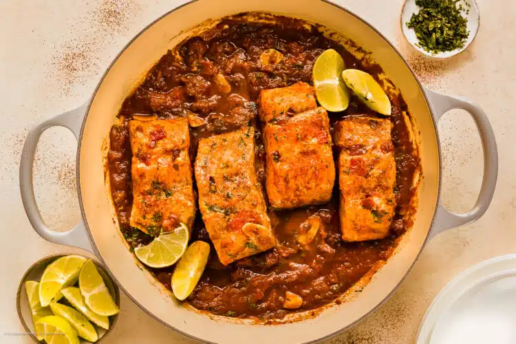 Overhead photo of four honey chipotle salmon fillets with adobo sauce in a large skillet.