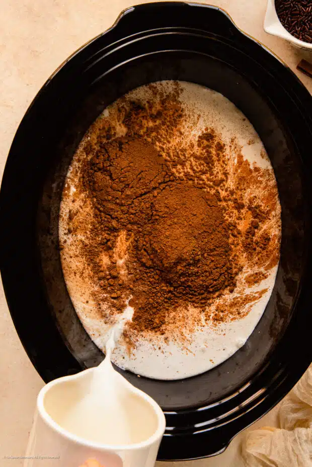 Action photo of milk being poured into a slow cooker with cocoa powder.