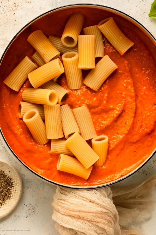 Overhead photo of a white pot with vodka sauce and pasta cut in half.
