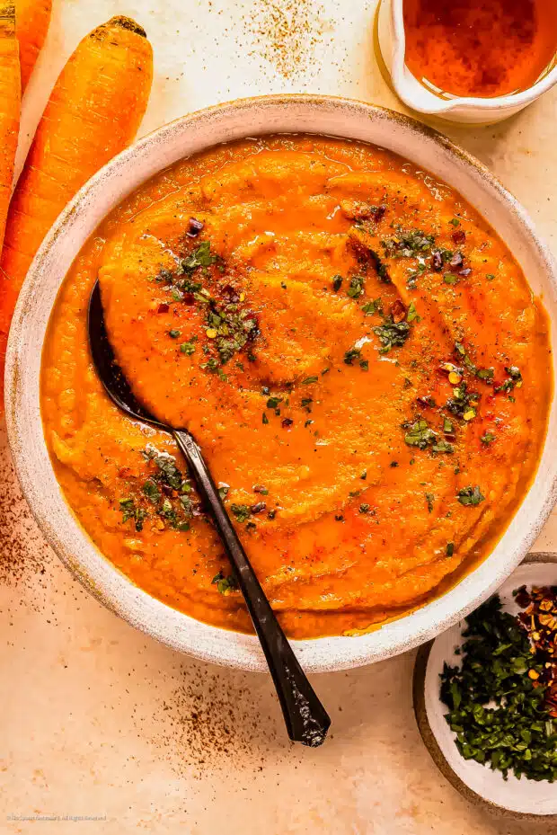 Overhead photo of a bowl of gingered carrot soup with a spoon inserted into the soup.