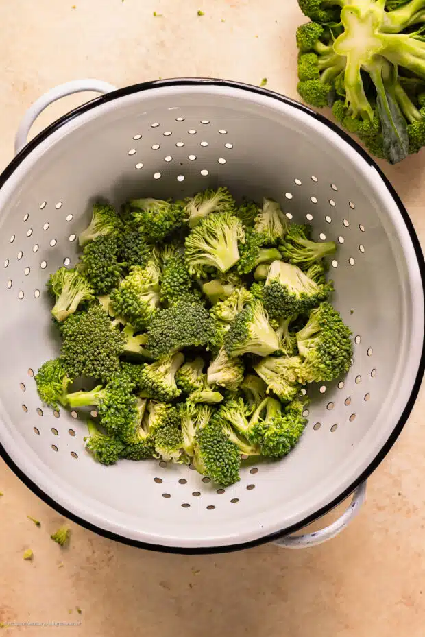 Action photo showing the preparation of broccoli florets draining in a colander before ricing.