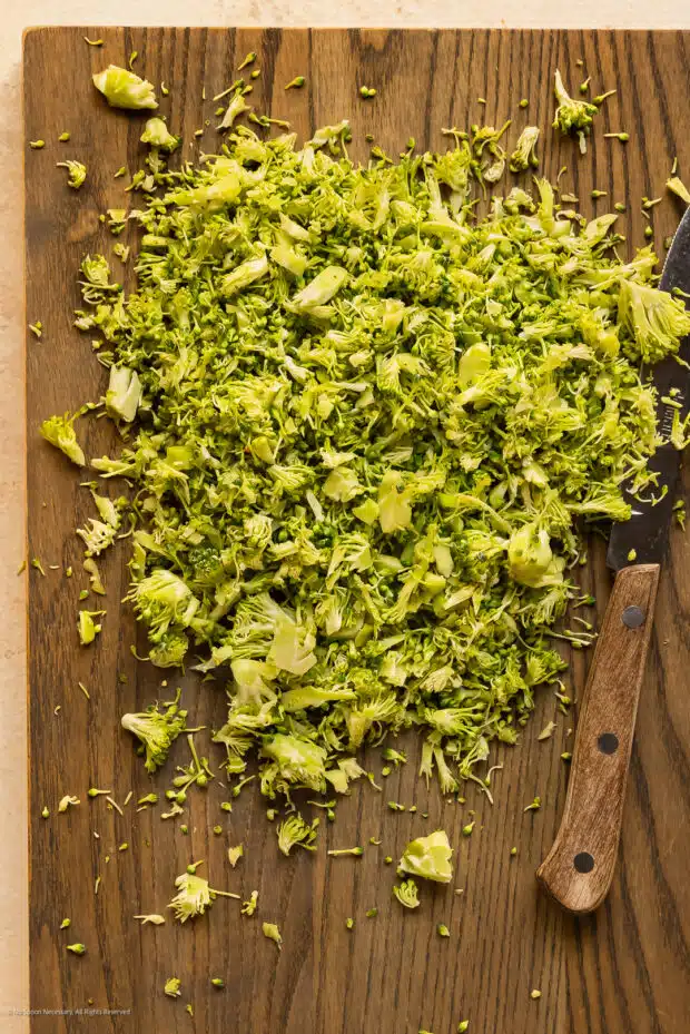 Overhead photo of riced broccoli on a wood cutting board with a kitchen knife.