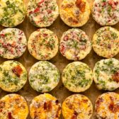 Overhead photo of twenty four egg breakfast muffins with various filling options neatly arranged on a wood serving board.