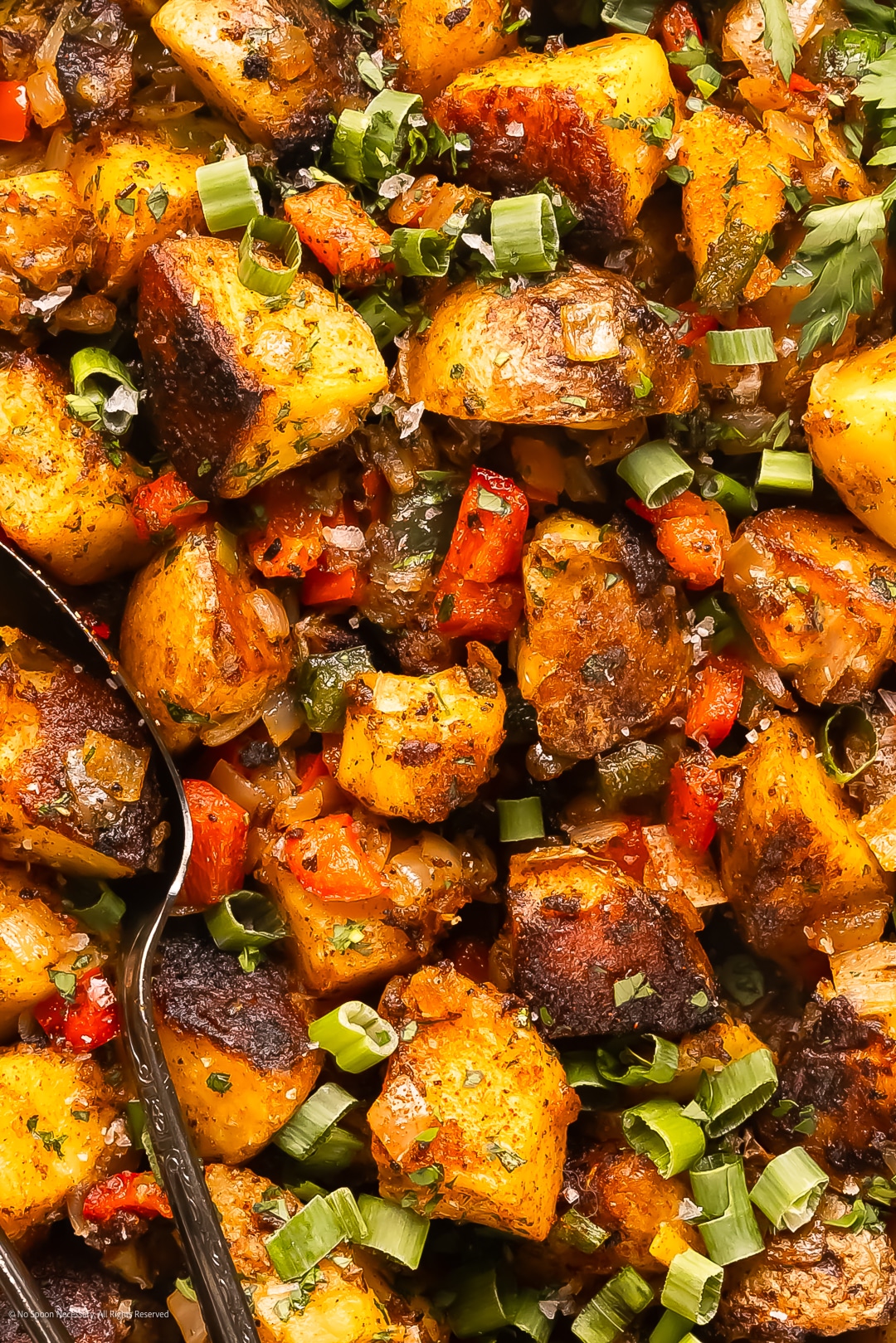 Close up photo of crispy diner home fries with red bell peppers, yellow onions, and poblano peppers.