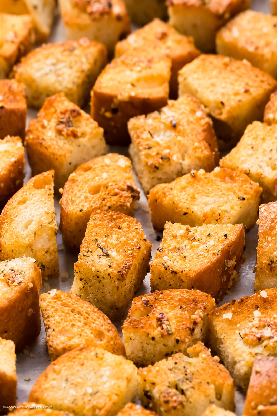 Close-up, angled photo of oven croutons cooling on a baking sheet.