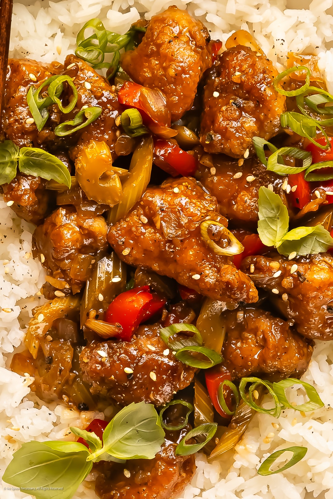 Close-up photo of crispy chinese peppercorn chicken garnished with fresh herbs and sesame seeds.